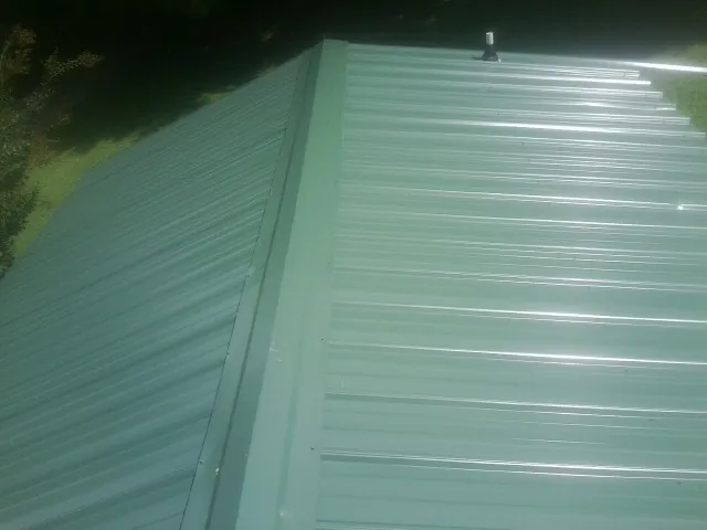 New green metal panels meeting at the ridge of a roof — Flat Roof Repair work by our crew in Leon
