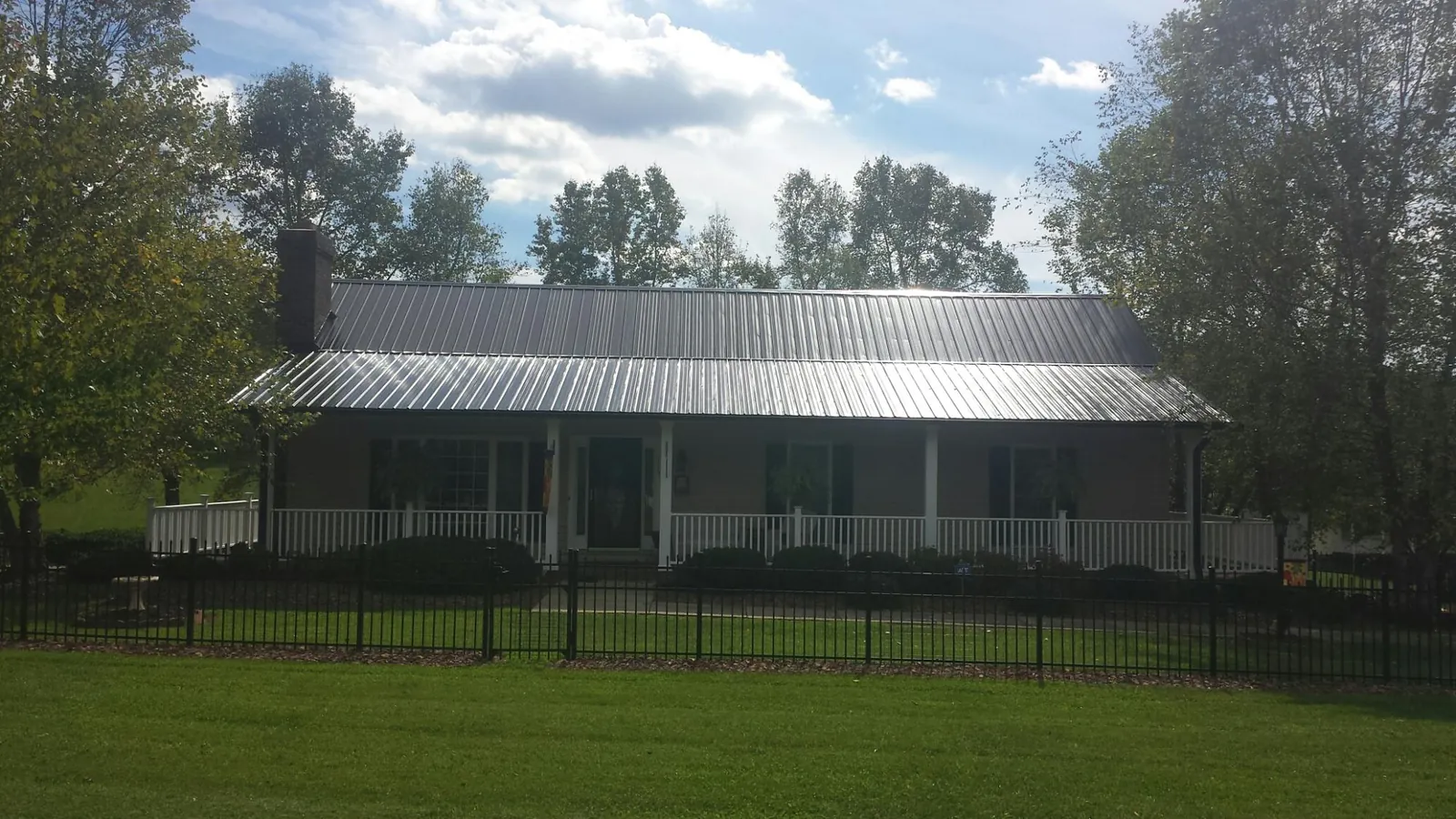 Gray metal roof on a brick ranch with a full width front porch — Gutter Guard Installation work by our crew in Leon