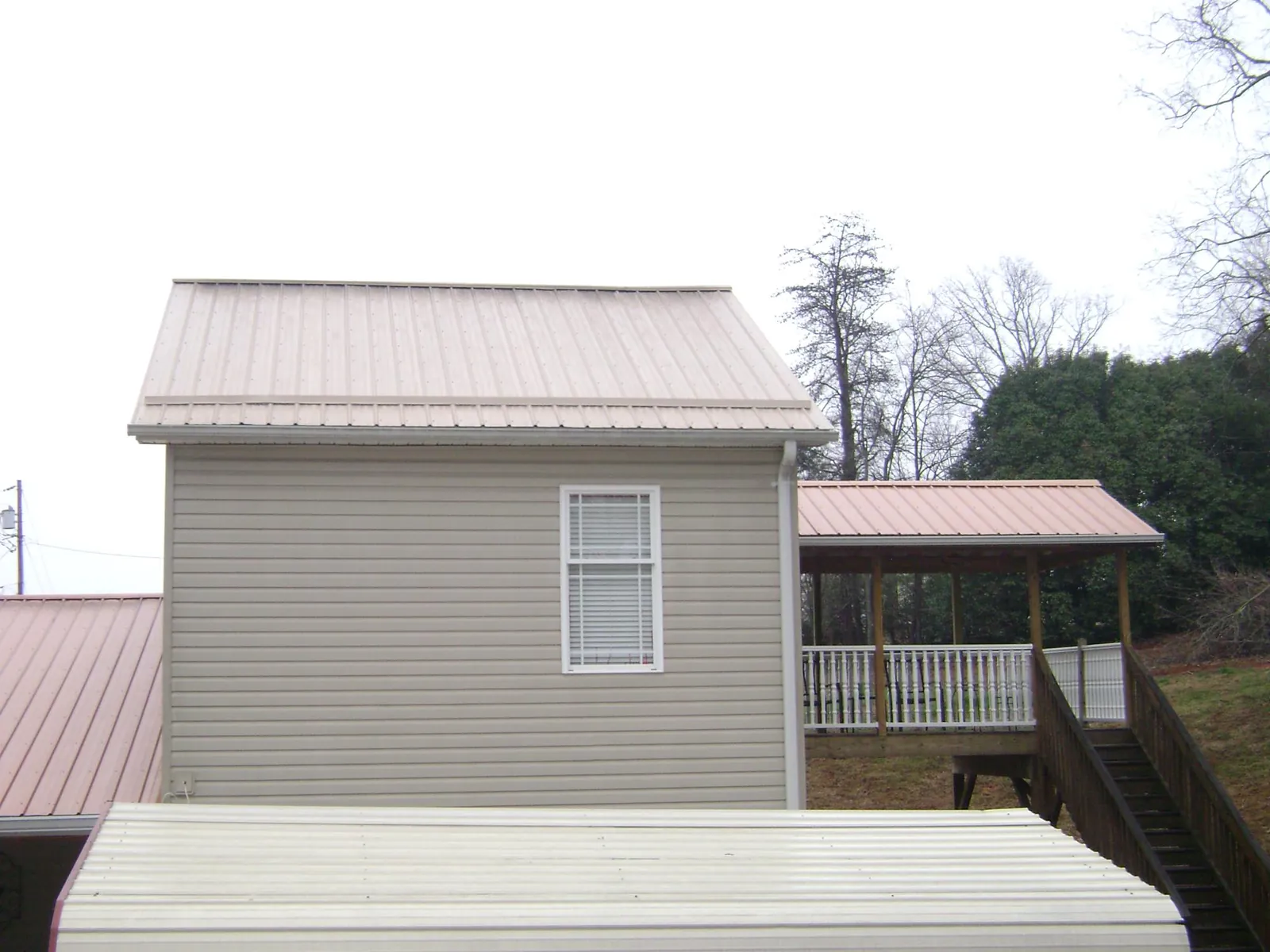 Tan metal roofs on a two story addition and attached porch, from a Roof Replacement job in Leon